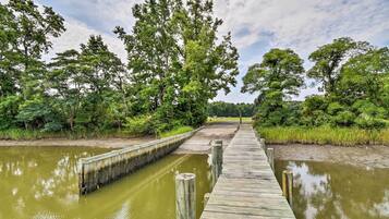 A wooden boardwalk over a calm water body, surrounded by dense greenery and trees.