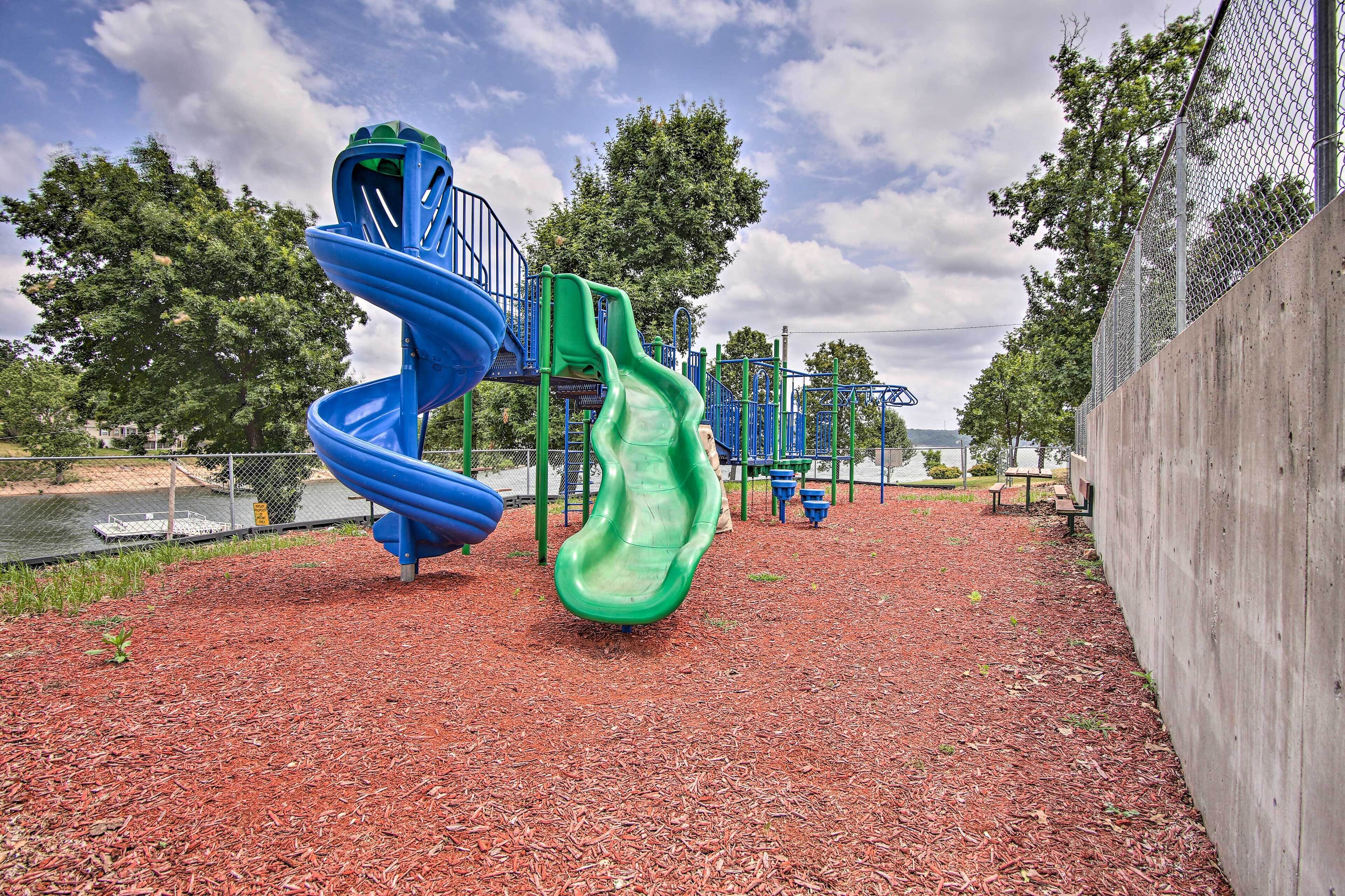 A playground with two slides, a fence, and trees in the background.