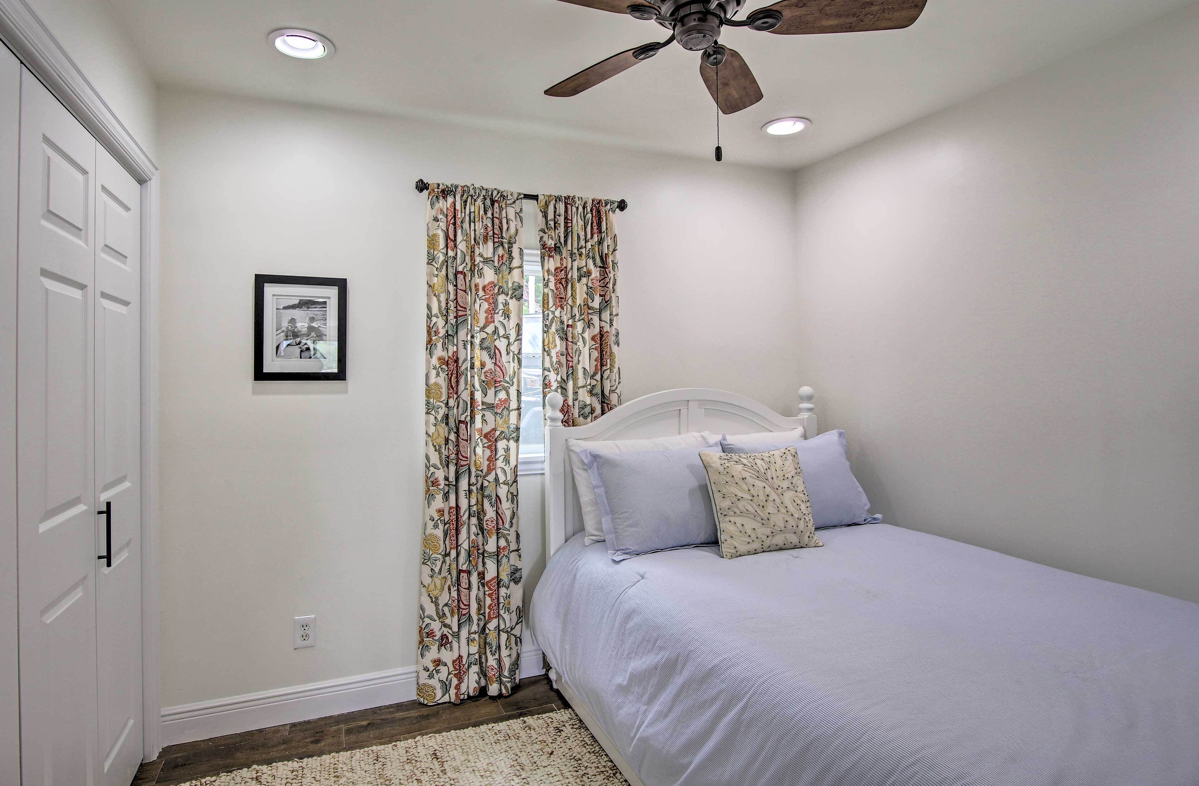 Un dormitorio con una cama individual, ventilador de techo y ventana con cortinas florales.