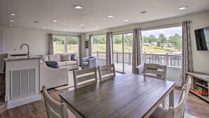 A spacious room with a wooden dining table, white upholstered sofas, and a large window with a view of a deck and greenery. - Walk to Boat Ramp! Lakefront Home w/ Deck in Afton (Afton)