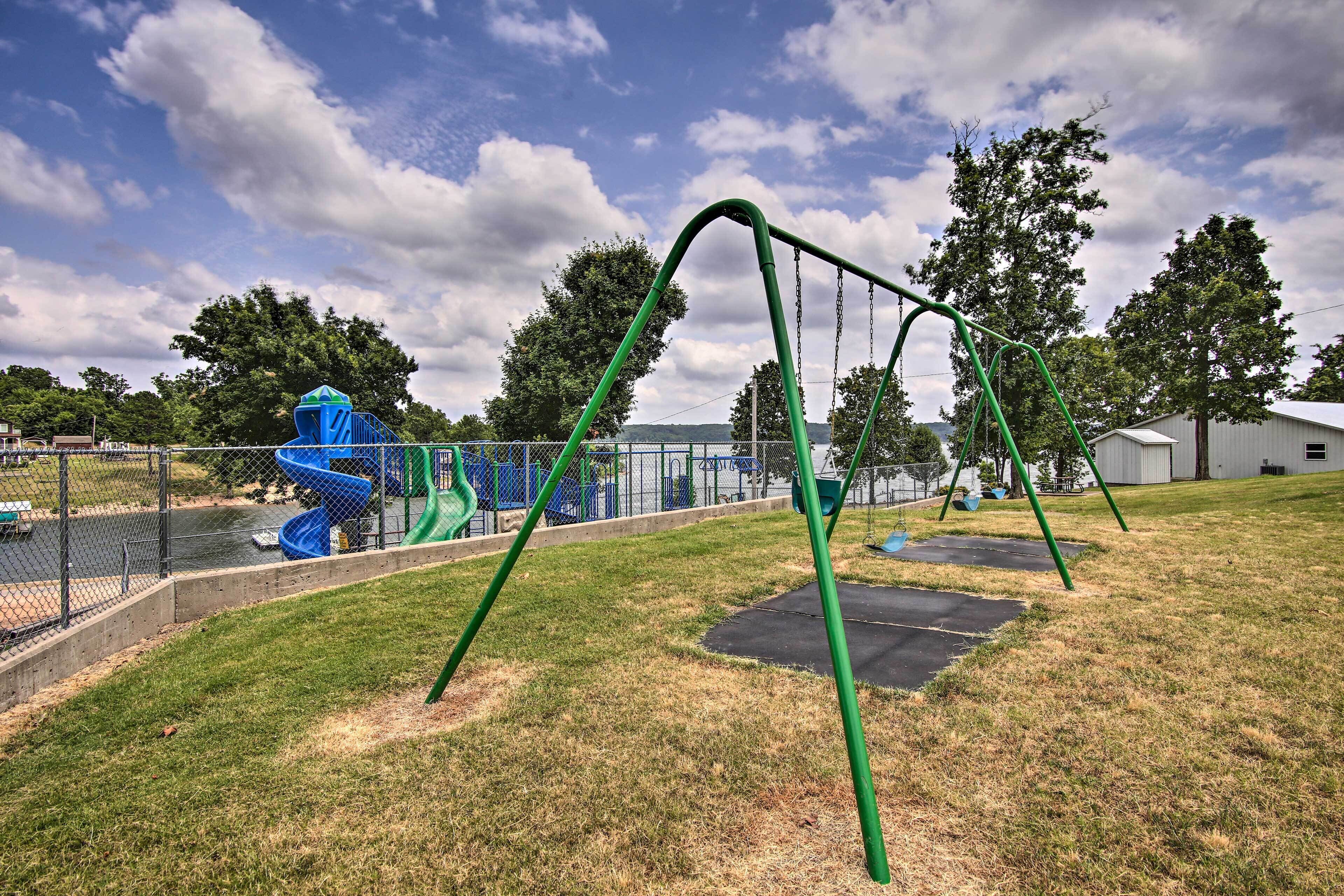 Un parque infantil con columpios y toboganes, rodeado de una valla y árboles.