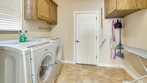 A laundry area with a front-loading washer and dryer, wooden cabinets, a door, and a broom rack.