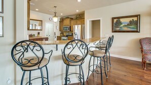 A kitchen with wooden cabinets, a stainless steel refrigerator, and a bar area with metal chairs.
