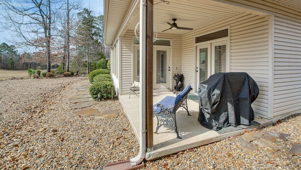 A covered porch with a ceiling fan, a grill, and a bench.