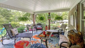 A covered outdoor seating area with wicker furniture, a decorative rug, and a view of the surrounding greenery. - Fire Pit & Game Room: Family Home in Marshall! (Weaverville)