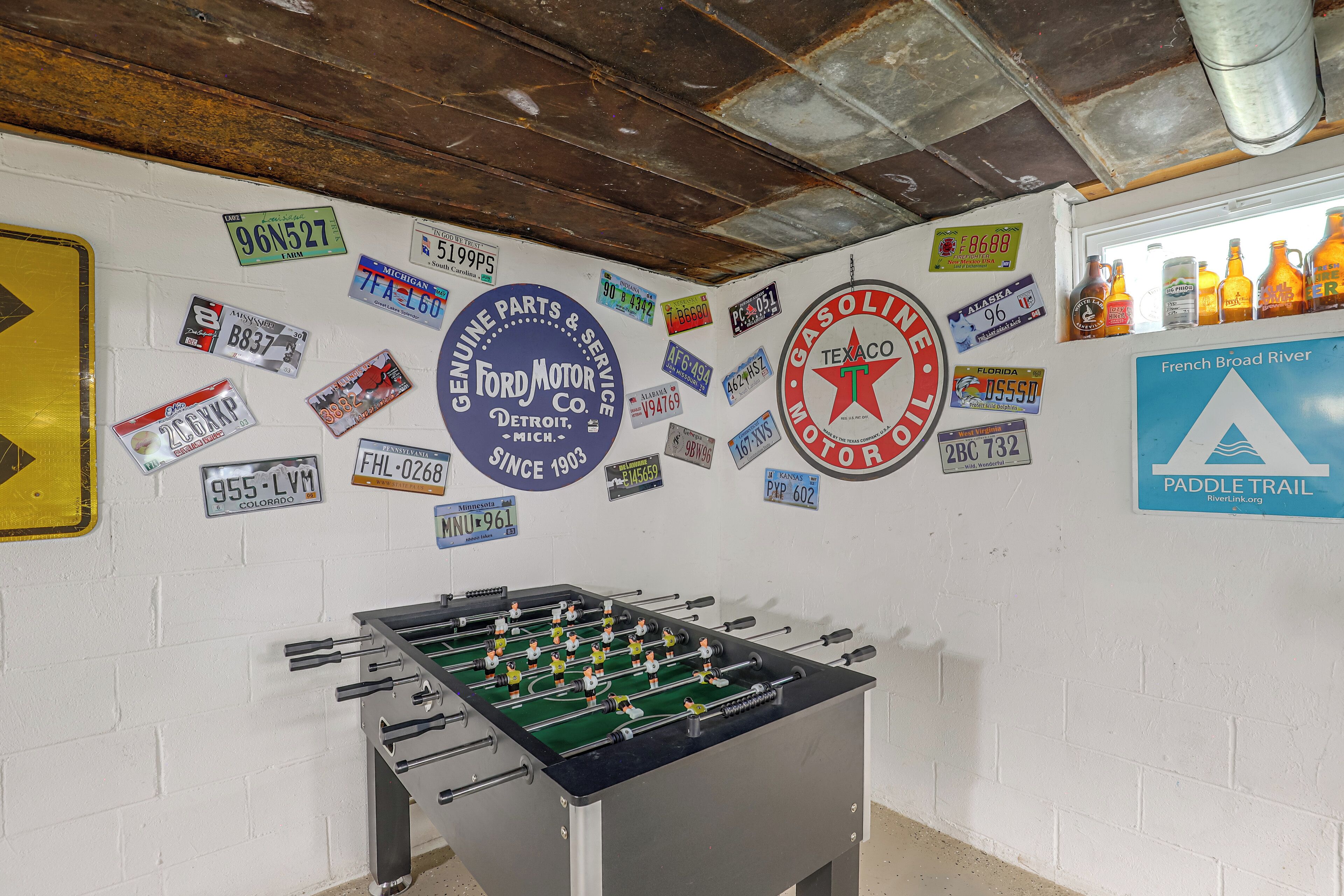 A room with a foosball table, a wall decorated with various license plates, and a sign for the French Broad River Paddle Trail.
