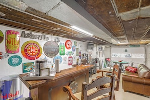A bar area with a wooden counter, various beer taps, and a wall adorned with brewery signs. - Fire Pit & Game Room: Family Home in Marshall! (Weaverville)