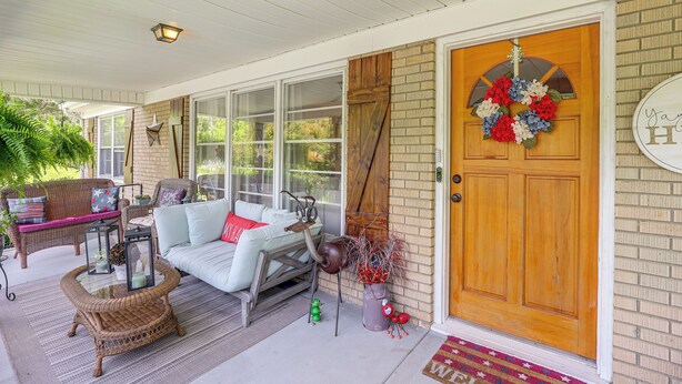 A covered porch with wicker furniture, a wooden door with a wreath, and a brick wall. - Fire Pit & Game Room: Family Home in Marshall! (Weaverville)