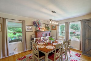A dining area with a wooden table, white chairs, and a hanging light fixture. - Fire Pit & Game Room: Family Home in Marshall! (Weaverville)