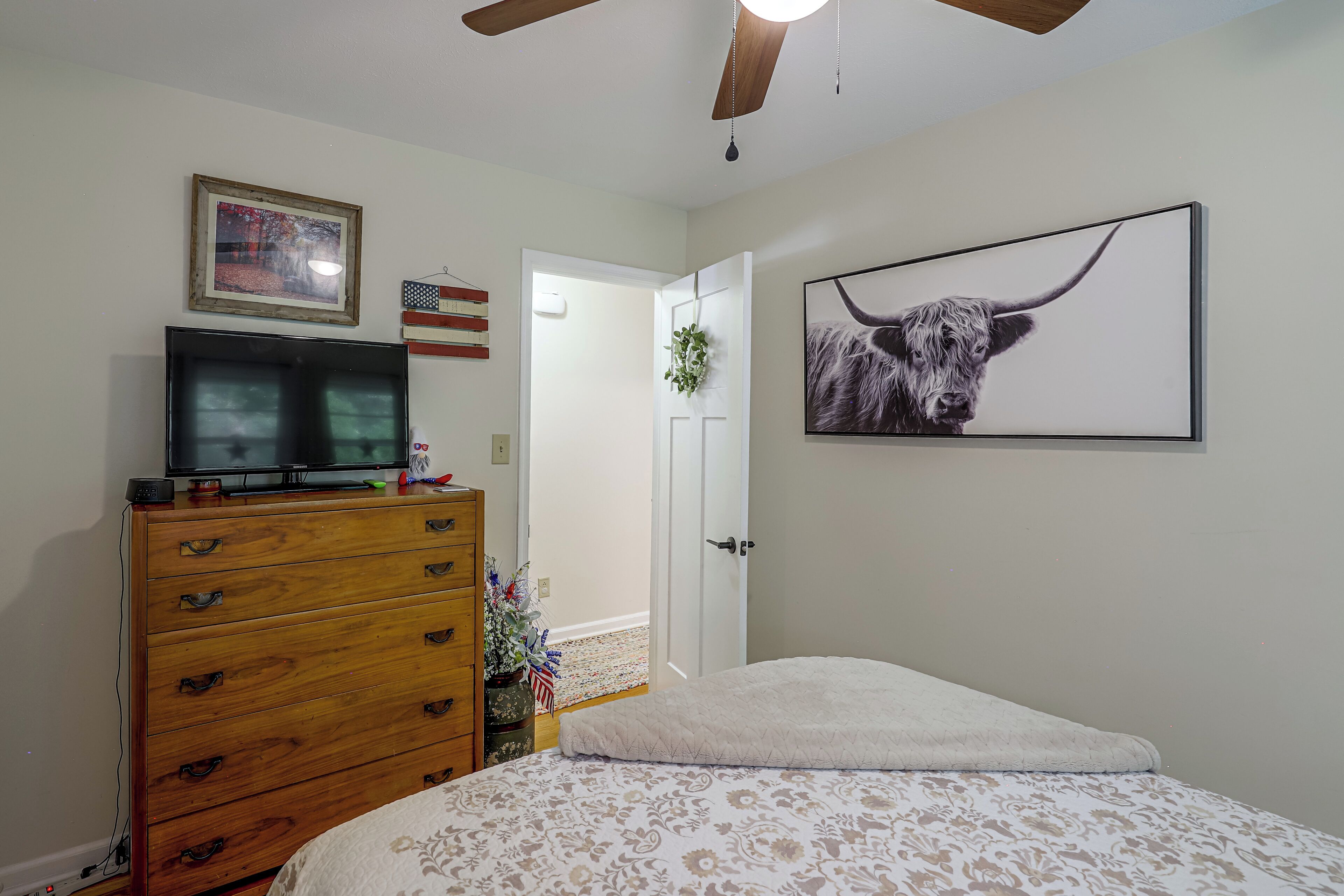 A bedroom with a bed, a dresser, a television on top, a framed picture, and a wall-mounted artwork of a bull.
