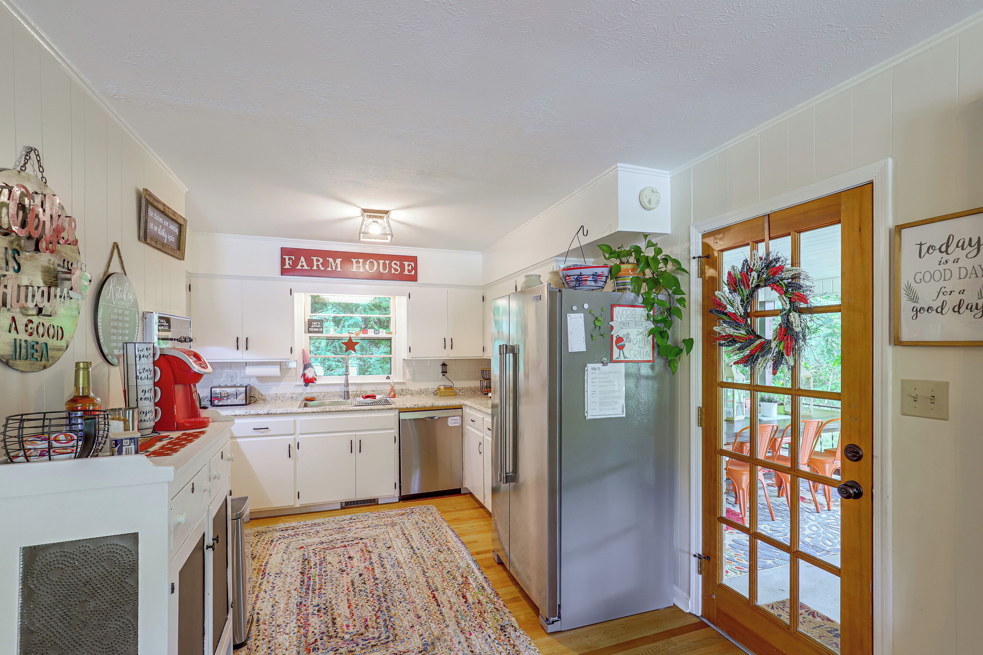 A kitchen with white cabinets, a stainless steel refrigerator, and a farmhouse sign.