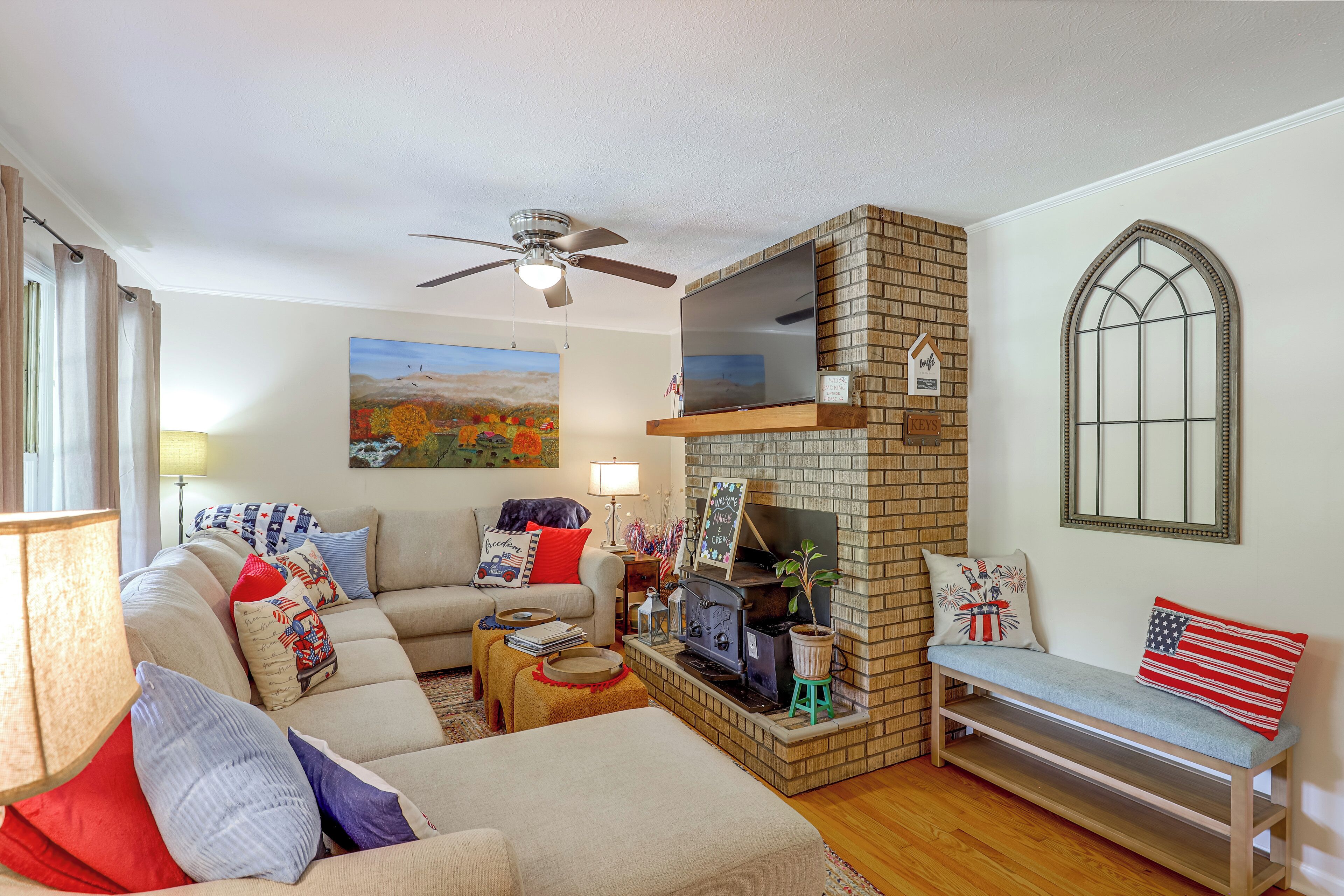 A living room with a fireplace, a ceiling fan, a couch, and a window with a decorative frame.