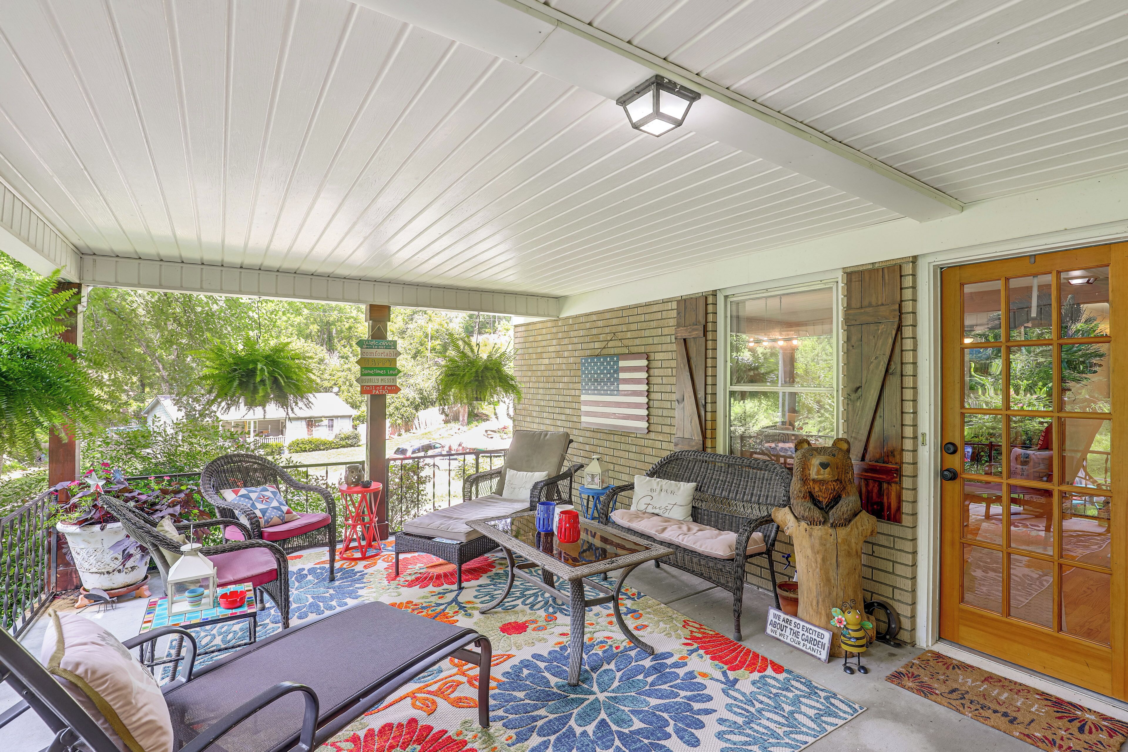 A covered outdoor seating area with wicker furniture, a colorful rug, and a view of the garden.
