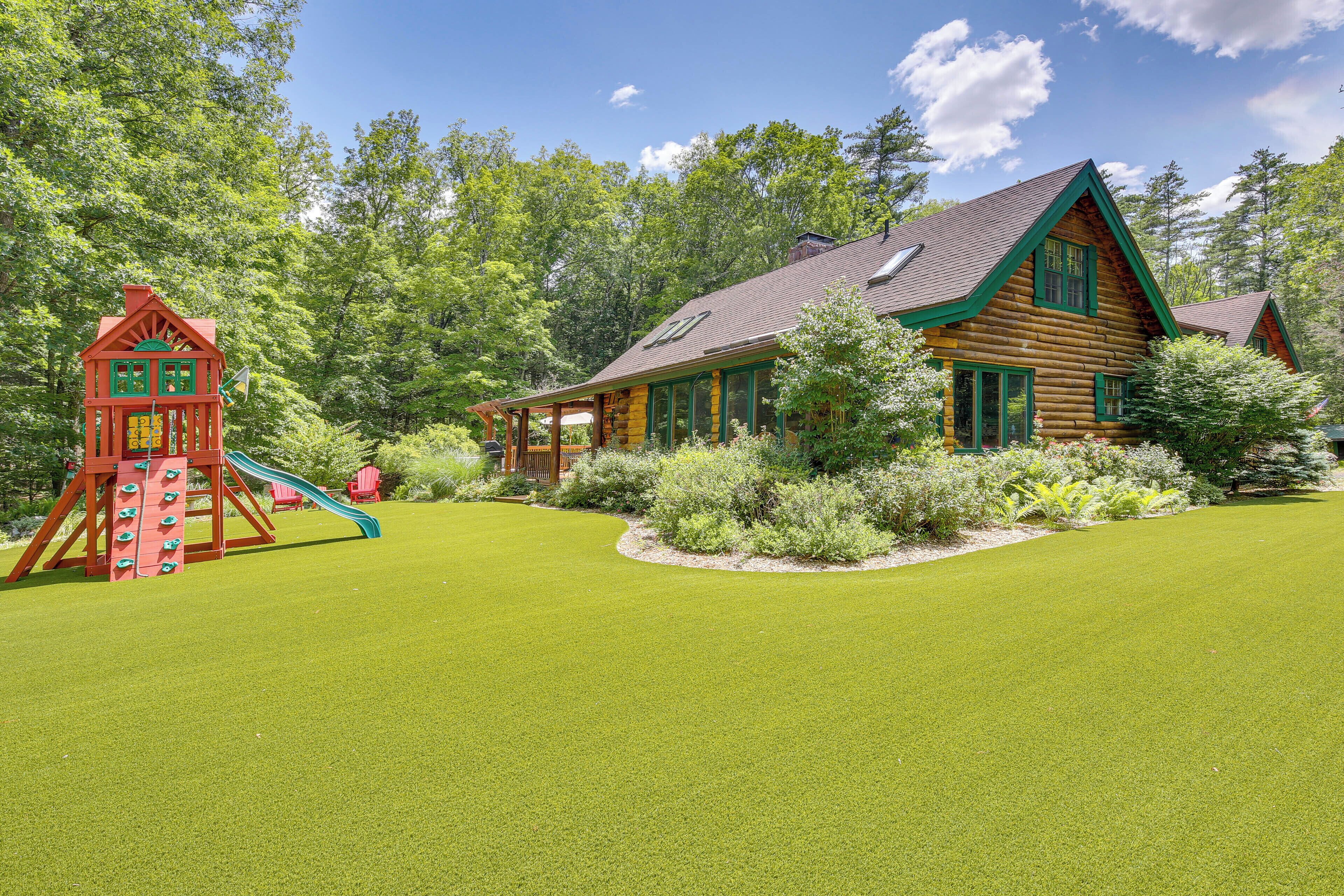 A log cabin with a green roof and a play area with a slide.