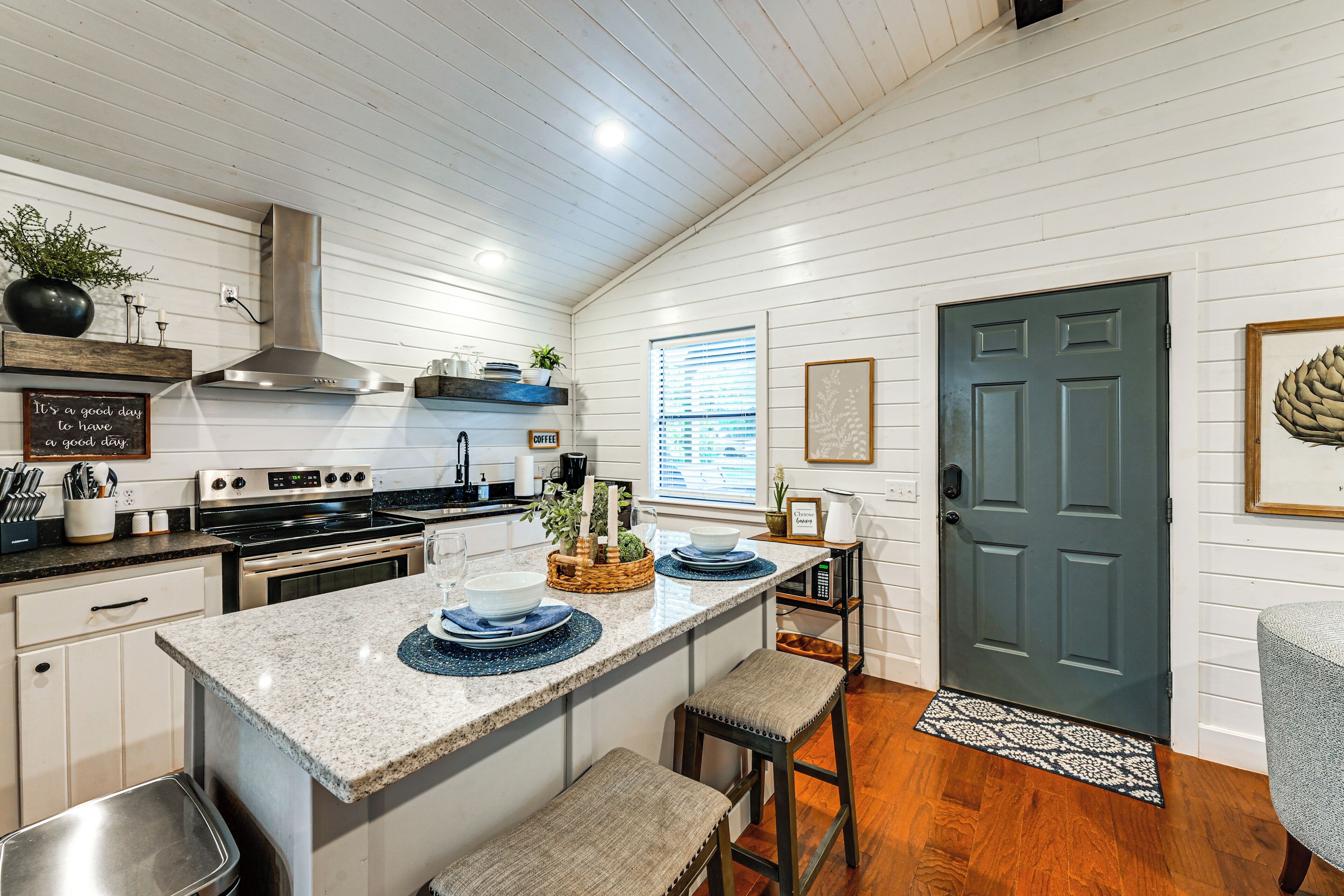 A kitchen with white wooden walls, a stainless steel range hood, a built-in oven, and a large island with blue placemats.