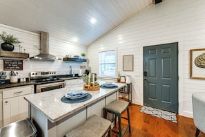 A kitchen with white wooden walls, a stainless steel range hood, a built-in oven, and a large island with blue placemats. - Serene Broken Bow Cabin w/ Fire Pit & Gas Grill! (Broken Bow)