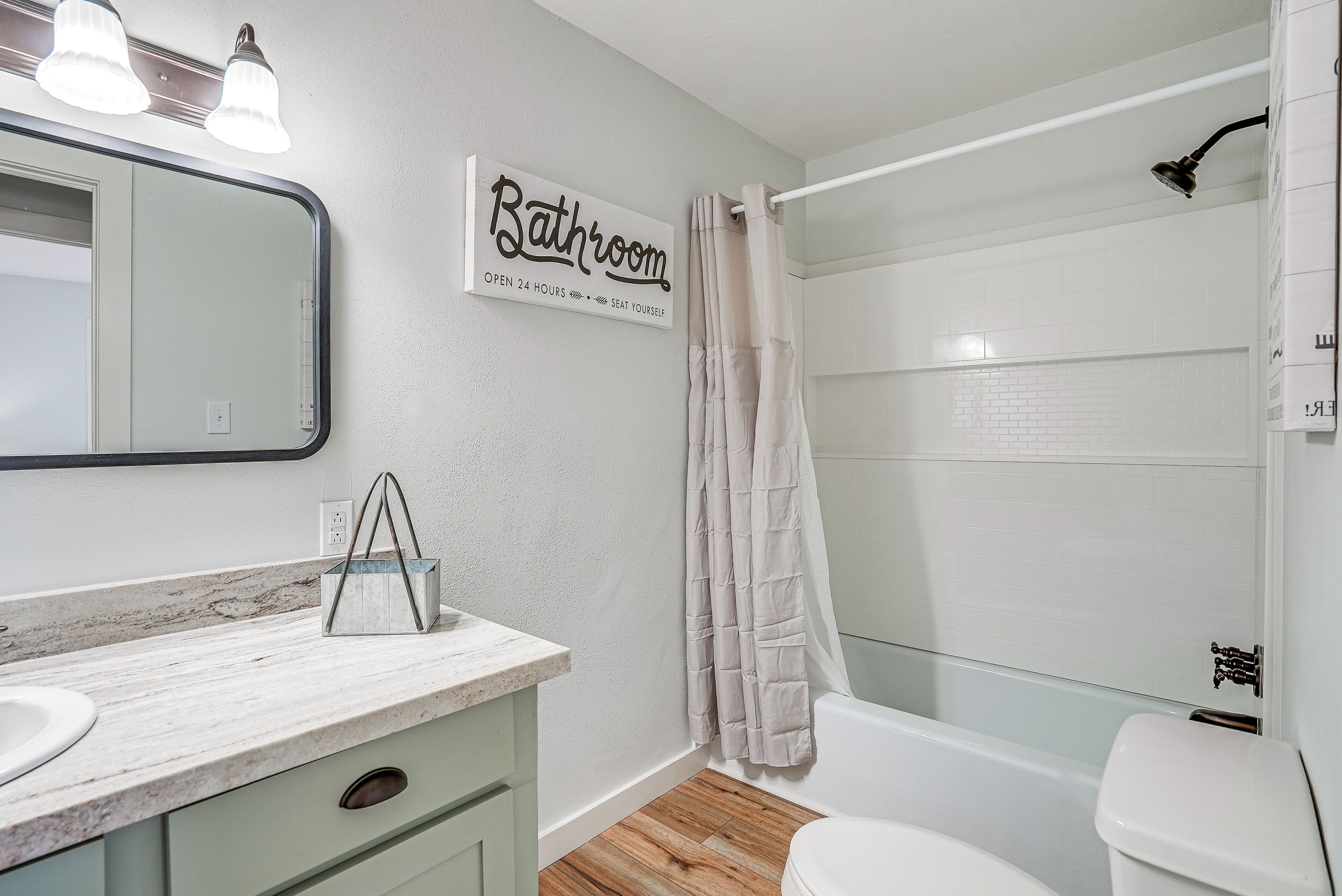 A bathroom with a white sink, mirror, and a sign that reads 'Bathroom Open 24 Hours Seat Yourself'.