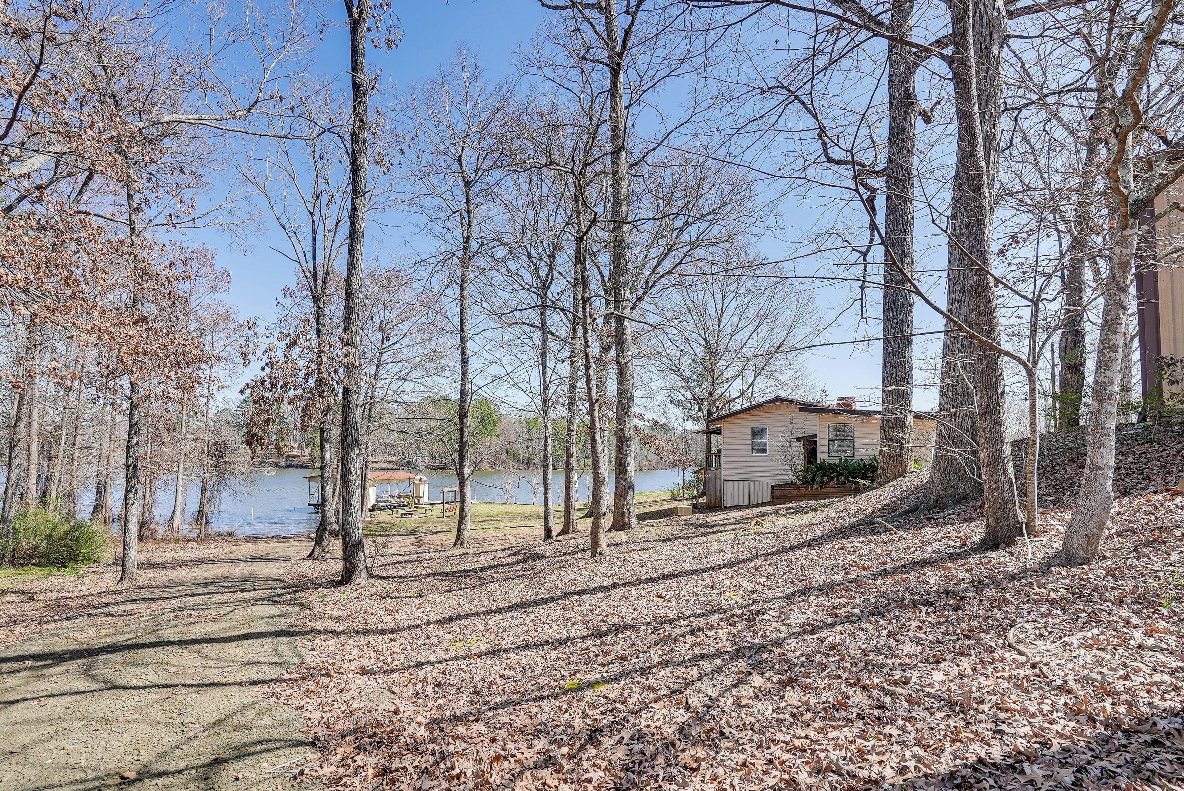 A lakeside property with a dirt path, leaf-covered ground, and a small building near the water.