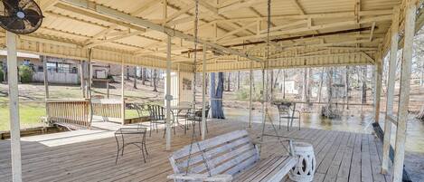 A covered outdoor area with a wooden bench, tables, chairs, and a fan.