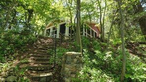 A stone staircase leading to a building with a red roof, surrounded by lush greenery and trees. - Island Cottage on Evans Lake: Boat Rental Required (Tipton)