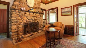 A stone fireplace with a mantel, a wooden ceiling, and a chandelier. There is a leather sofa and a wooden table in the room. - Island Cottage on Evans Lake: Boat Rental Required (Tipton)