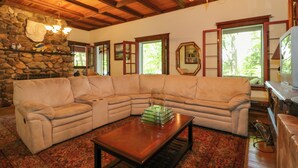 A living room with a beige sectional sofa, a wooden coffee table, and a stone fireplace. - Island Cottage on Evans Lake: Boat Rental Required (Tipton)