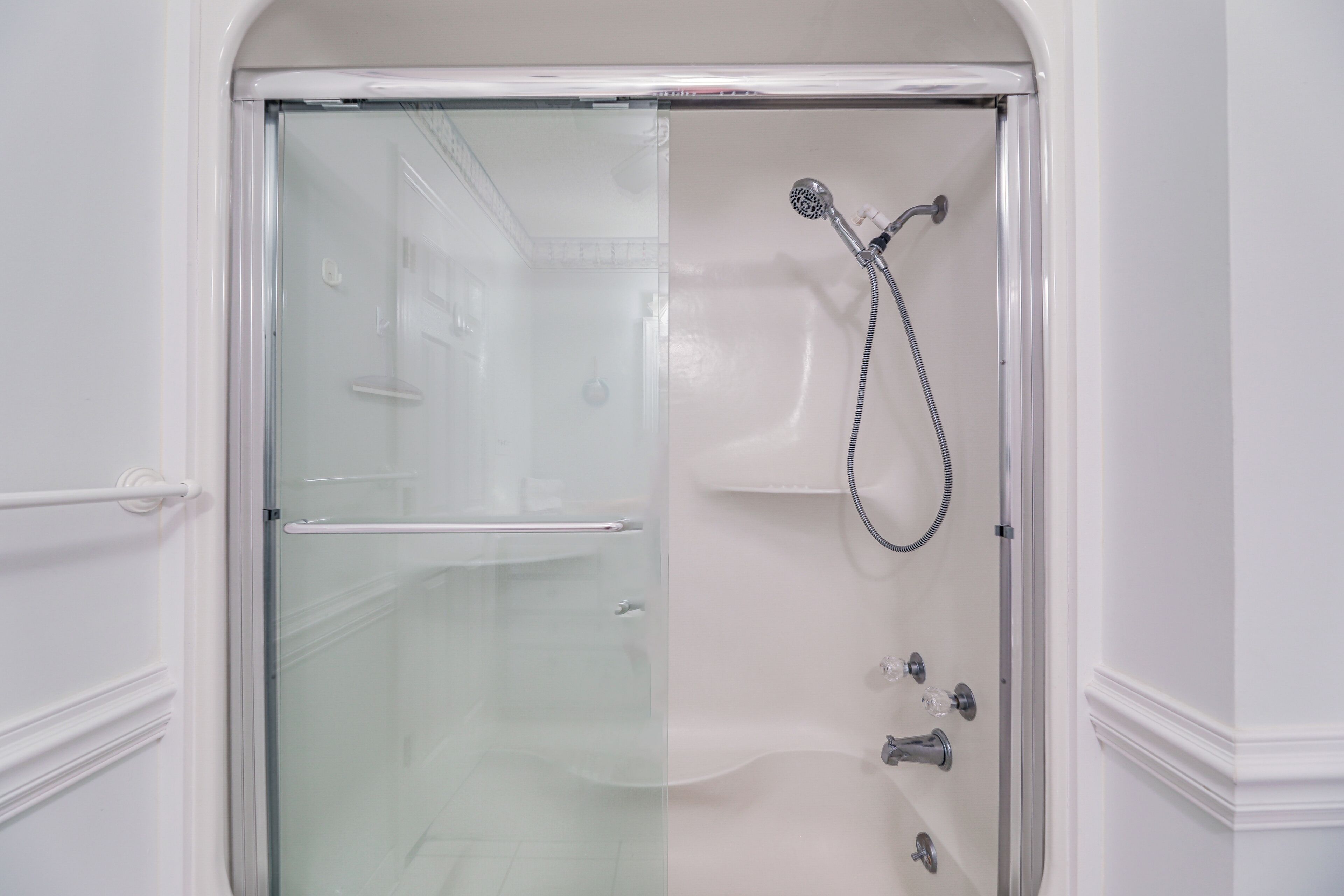 A glass-enclosed shower stall with a handheld showerhead and a handheld faucet.