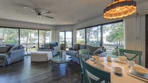 Un vaste espace de vie agrémenté d’un ventilateur de plafond, de grandes fenêtres et d’une table à manger pouvant accueillir quatre personnes.