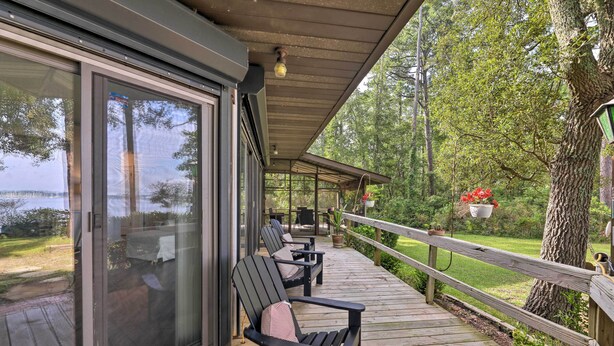 Une terrasse couverte, dotée de chaises et d’une table, qui offre une vue sur un lac et est entourée d’arbres.