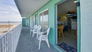 A balcony with white plastic chairs, a view of the beach, and a room with a blue door and a ceiling fan. - Updated Oceanside Condo - 5 Miles to Cape May! (Wildwood Crest)