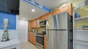 A kitchen with wooden cabinets, stainless steel appliances, and a wicker shelf. - Updated Oceanside Condo - 5 Miles to Cape May! (Wildwood Crest)