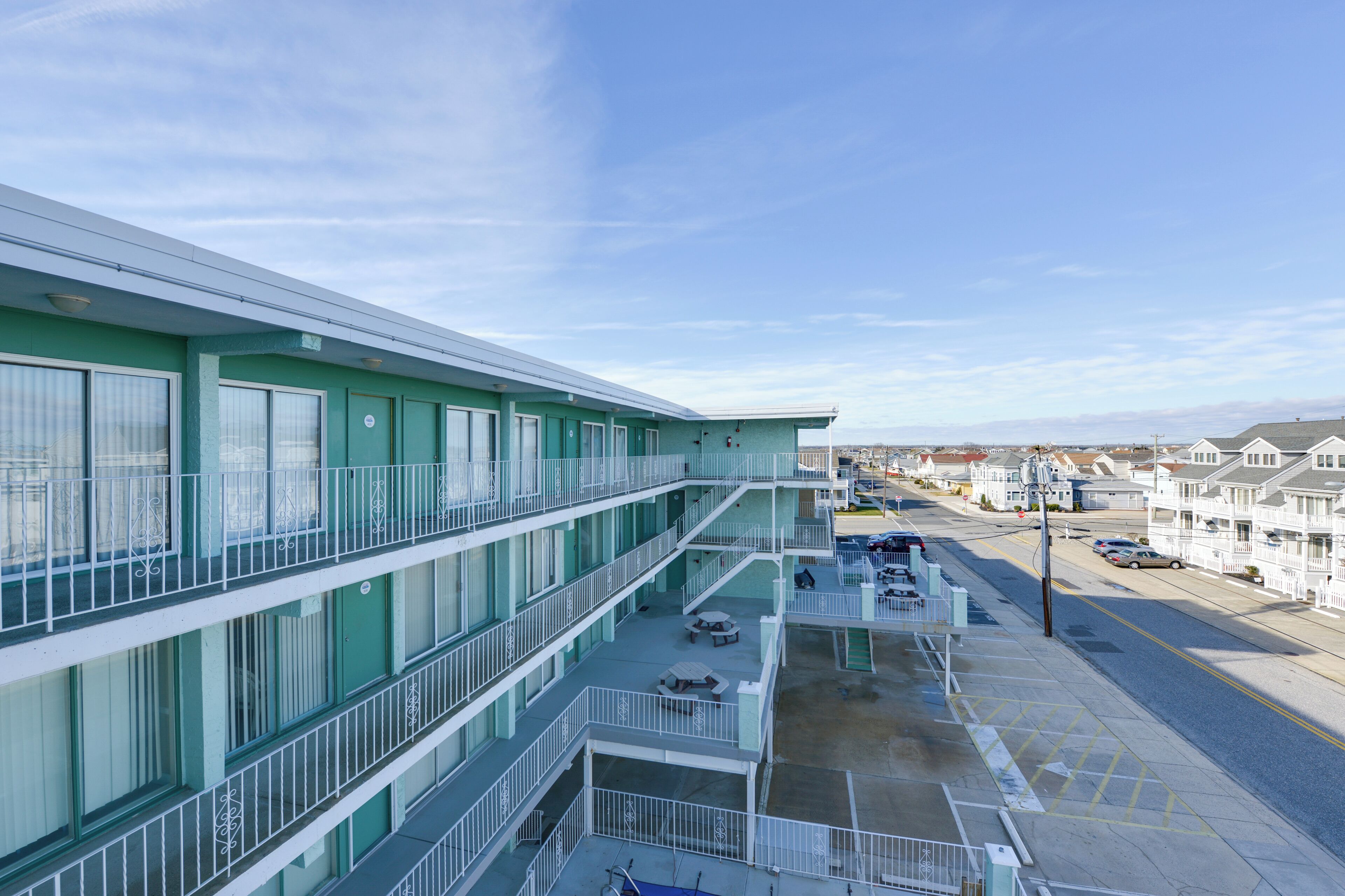 A multi-story hotel with balconies, outdoor seating, and a parking area.