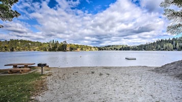 A lakeside picnic area with a bench and a picnic table, surrounded by trees and a clear sky.