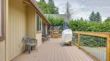 A wooden deck with a covered picnic table and chairs, a covered grill, and a view of the surrounding greenery.