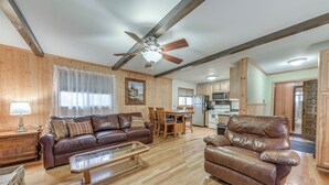 A spacious living room with a brown leather sofa, a wooden coffee table, and a brown leather armchair. A ceiling fan and a dining area with wooden chairs and a table are visible.