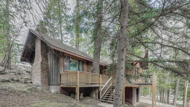 A cabin with a wooden deck and stairs leading to a second level.