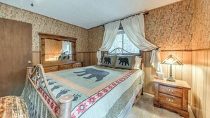 A bedroom with a bed, a wooden nightstand, a dresser, a mirror, and a window with curtains.