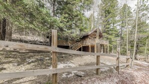A wooden cabin with a staircase leading to a deck, surrounded by trees.
