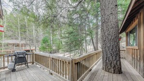 A wooden deck with a grill, a tree, and a wooden railing.