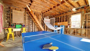 A ping pong table with two paddles and a ball, a wooden staircase, and a wooden wall with a window. - < 4 Mi to Cooperstown: Charming Historic Home! (Fly Creek)