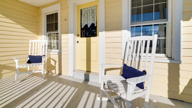 A porch with two white chairs, one with a blue cushion, and a yellow door with a decorative glass panel. - < 4 Mi to Cooperstown: Charming Historic Home! (Fly Creek)