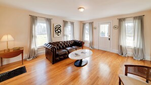 A spacious living room with a leather sofa, a round coffee table, and a wooden floor. - < 4 Mi to Cooperstown: Charming Historic Home! (Fly Creek)