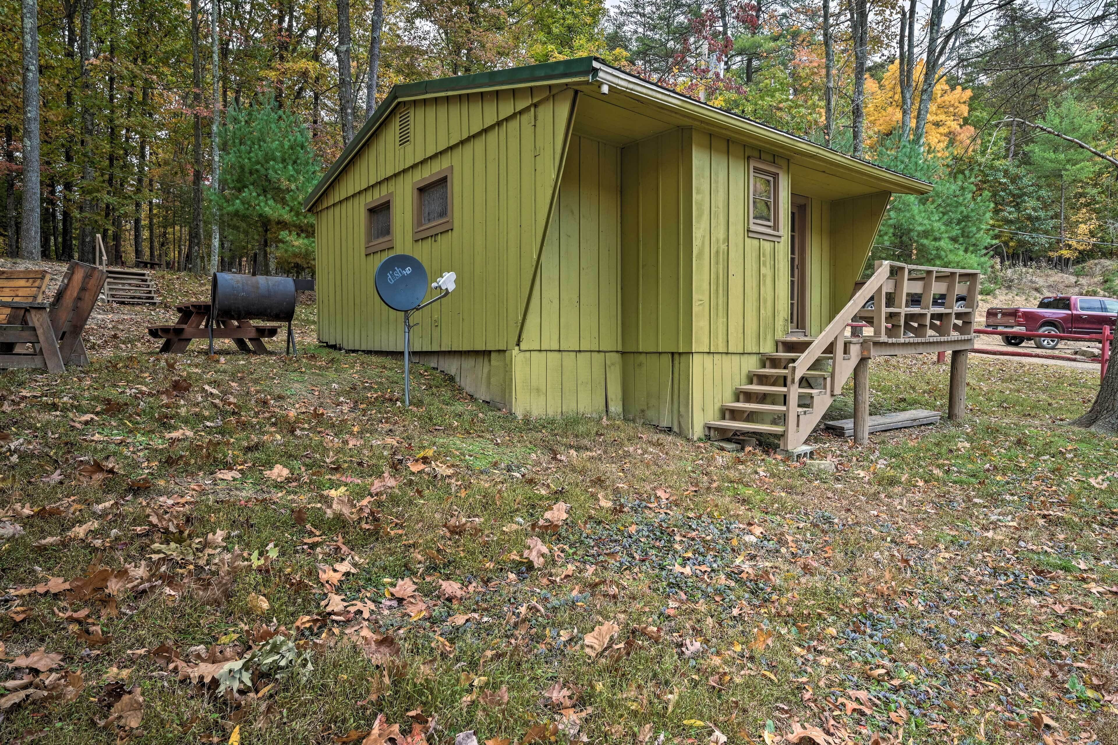 A small, single-story cabin with a green exterior, a wooden deck, and a mailbox.