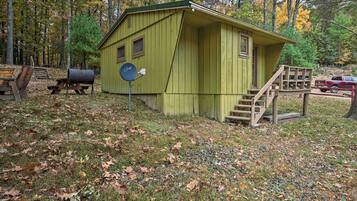A small, single-story cabin with a green exterior, a wooden deck, and a mailbox.
