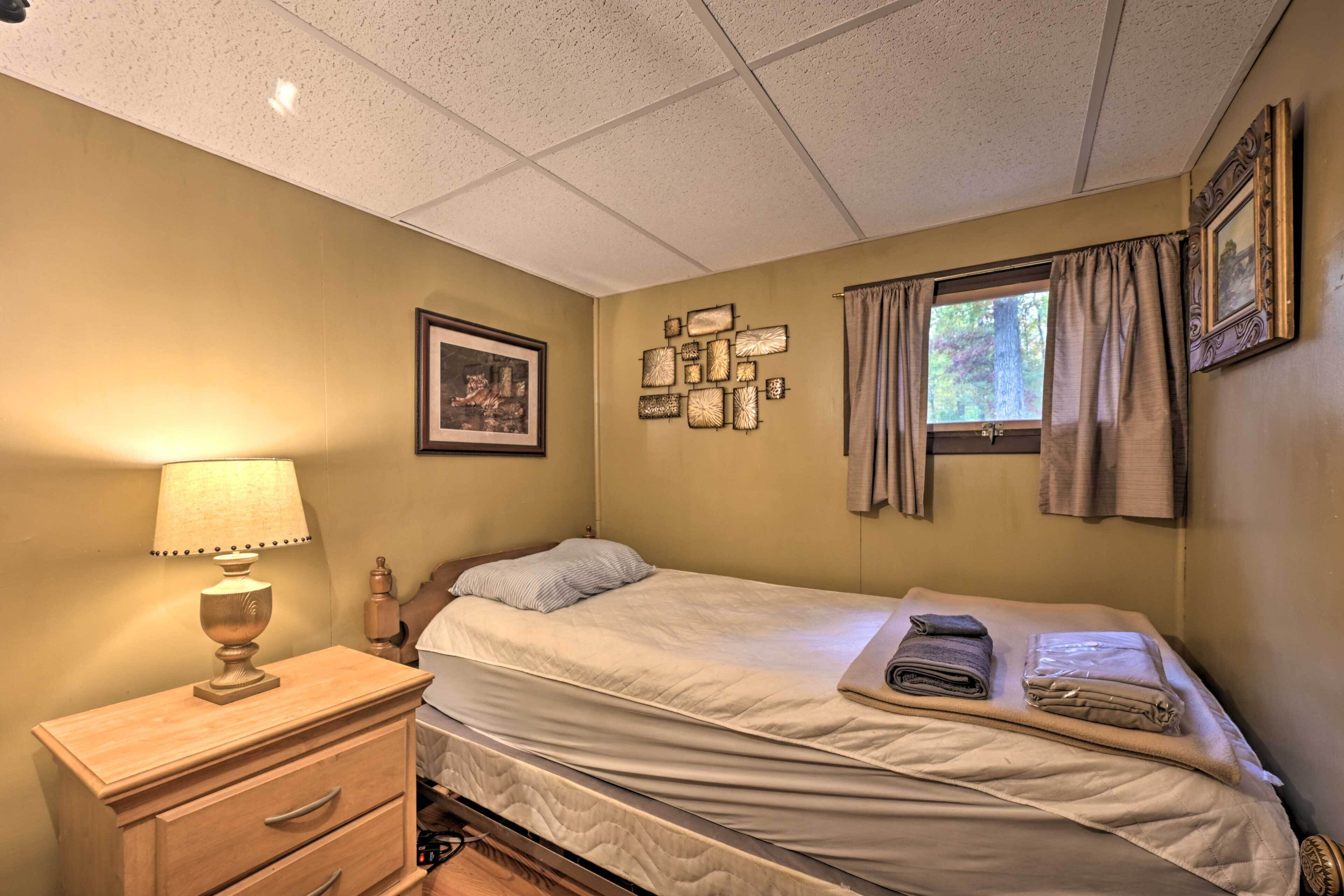 A bedroom with a bed, a nightstand with a lamp, a dresser, a window with curtains, and wall-mounted decor.