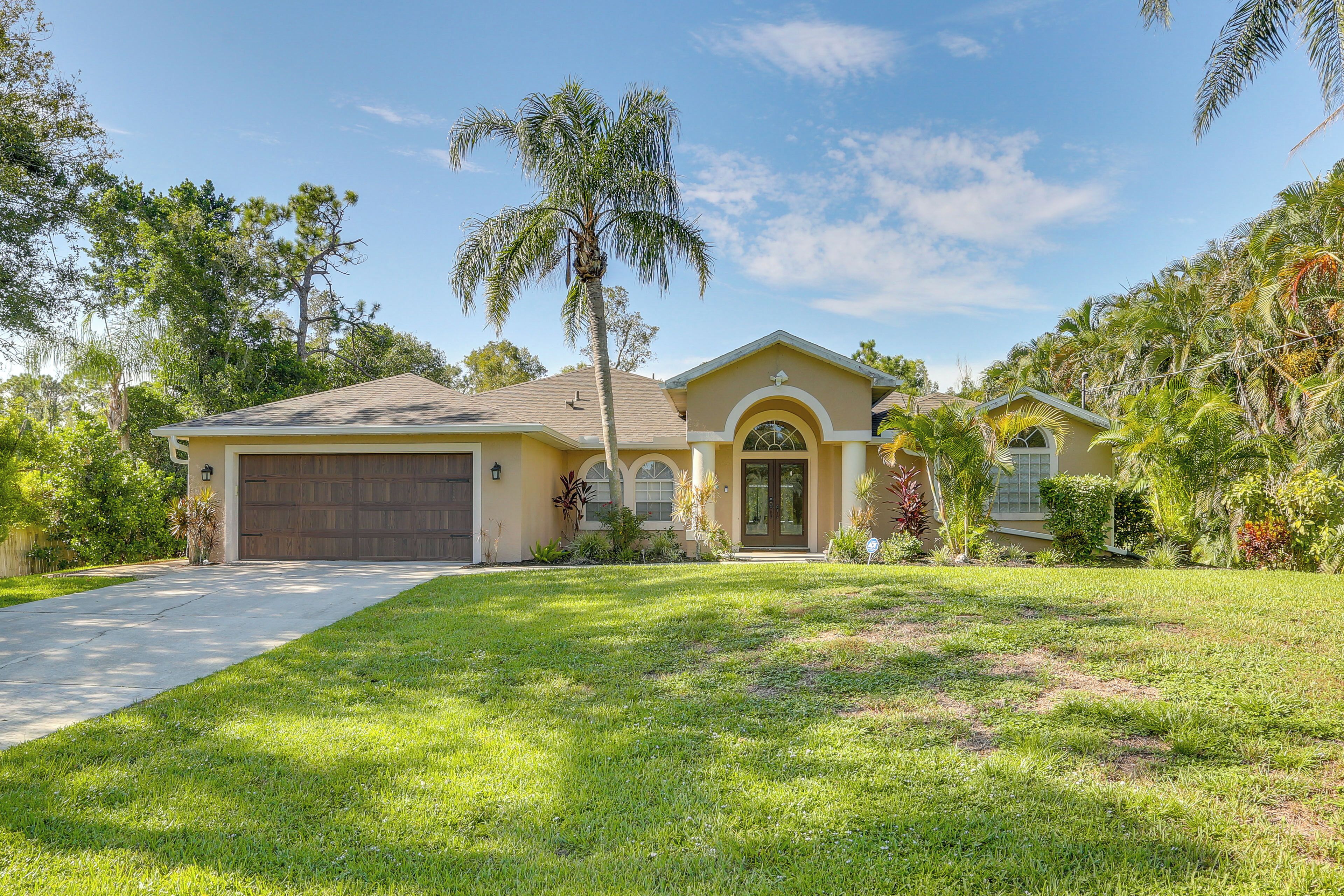 A two-story house with a front garage, a well-maintained lawn, and a variety of tropical plants.