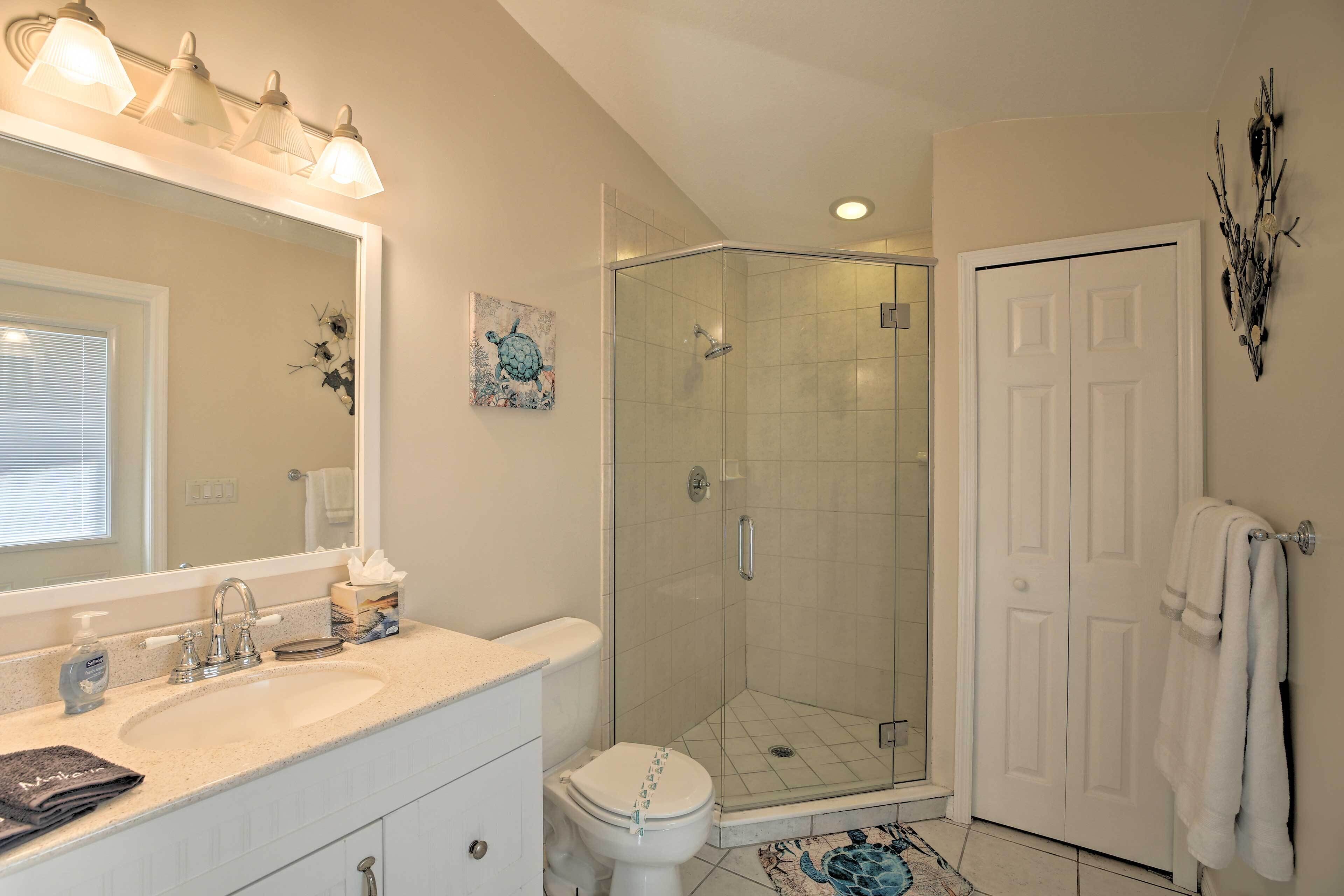 A bathroom with a glass shower enclosure, a white toilet, a sink with a mirror, and a towel rack.