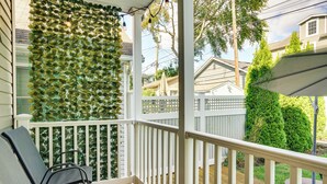 A wooden deck with white railings, a green wall with hanging lights, and a chair.