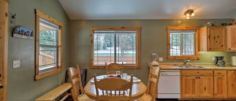A dining area with a wooden table and chairs, a bench, and a view of the outside through large windows.