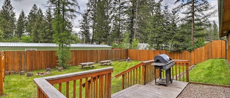 A wooden deck with a barbecue grill, picnic tables, and a wooden fence.